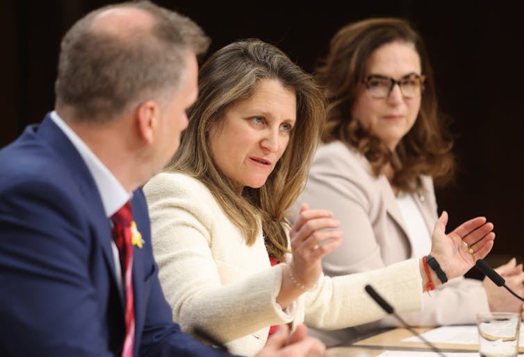 A woman talking and polluted with her hands written by a man and a woman with a table with microphone