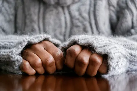 Electric verbs is a picture of hands of hands in FISTS, rest in a wooden area. The person wearing a blue jumper with its pants rid in around human cooks. 